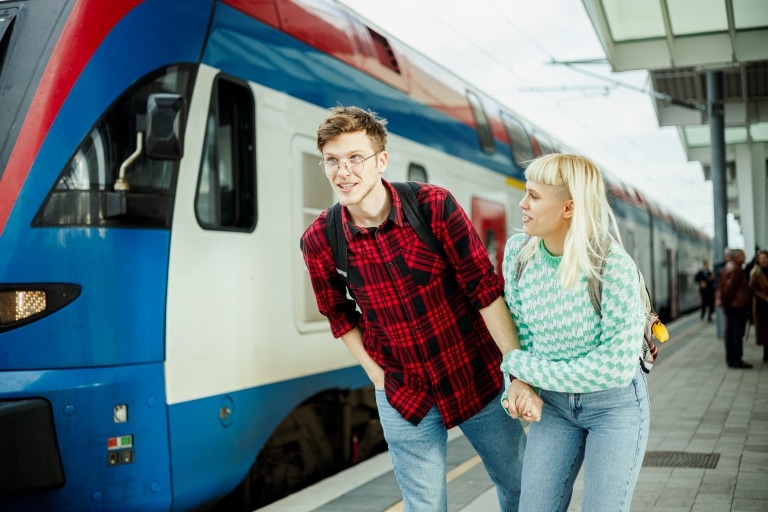 Zwei Jugendliche, männlich und weiblich, auf dem Bahnsteig, dahinter ein Zug