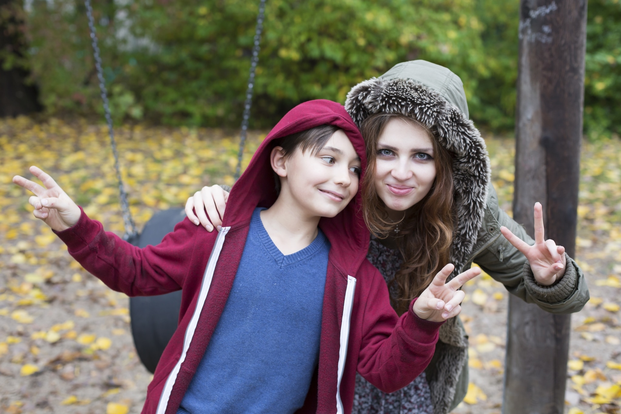 Au-pair-Mädchen und kleiner Junge am Spielplatz, die beide das Peace-Zeichen mit den Händen zeigen.