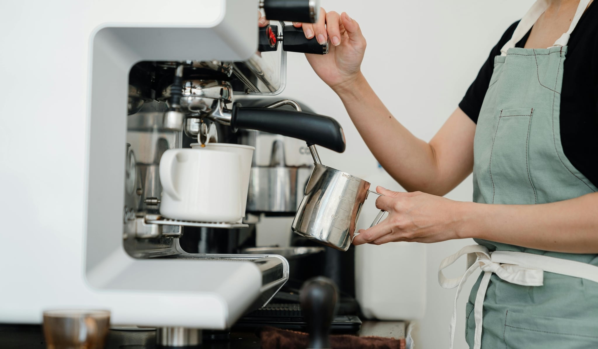 Junge Frau an der Kaffeemaschine, die Milch aufschäumt. Nur Hände und Oberkörper ist sichtbar