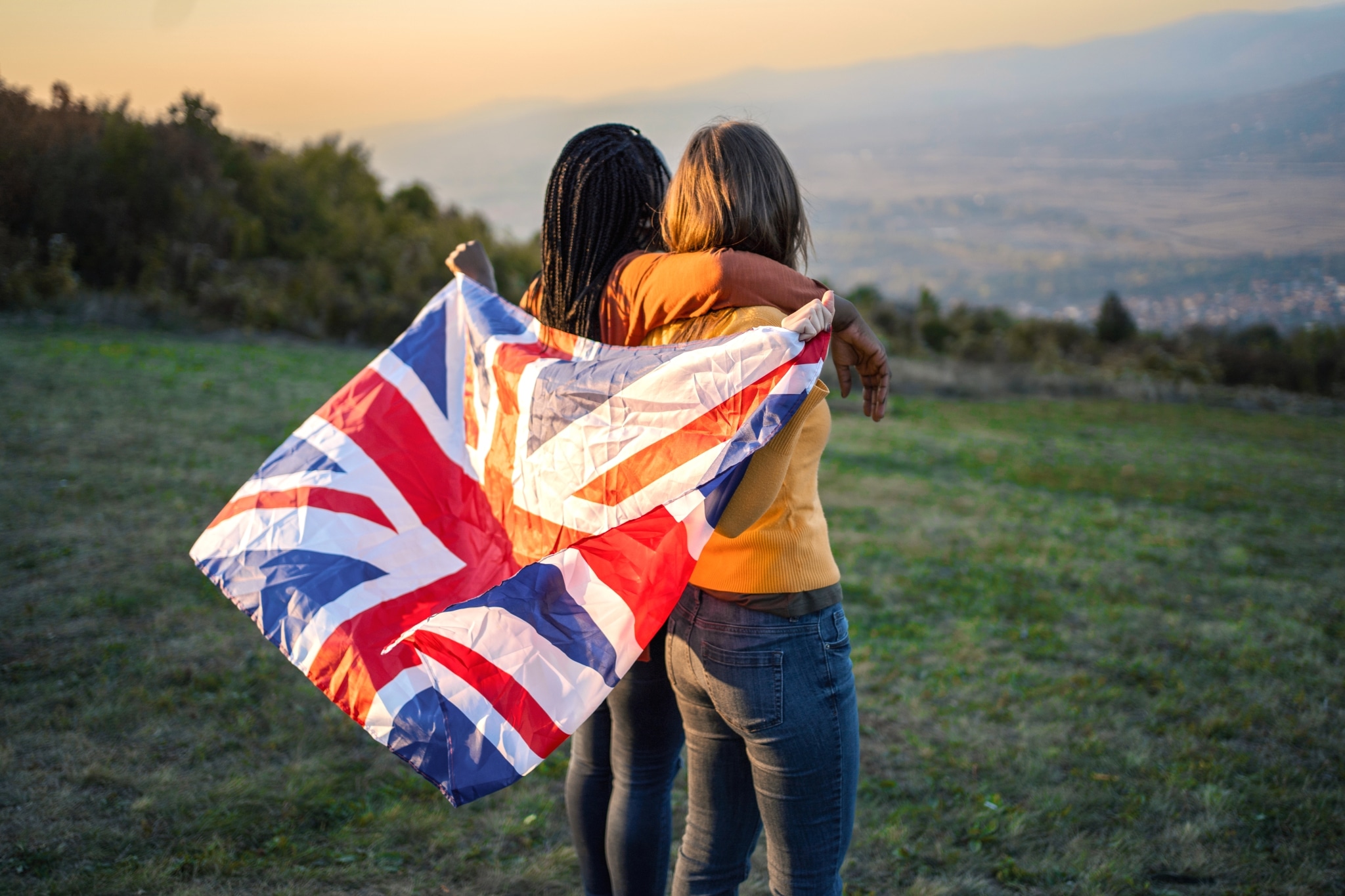 Zwei Frauen, die auf einem Hügel stehen und die britische Flagge hinter dem Rücken halten.