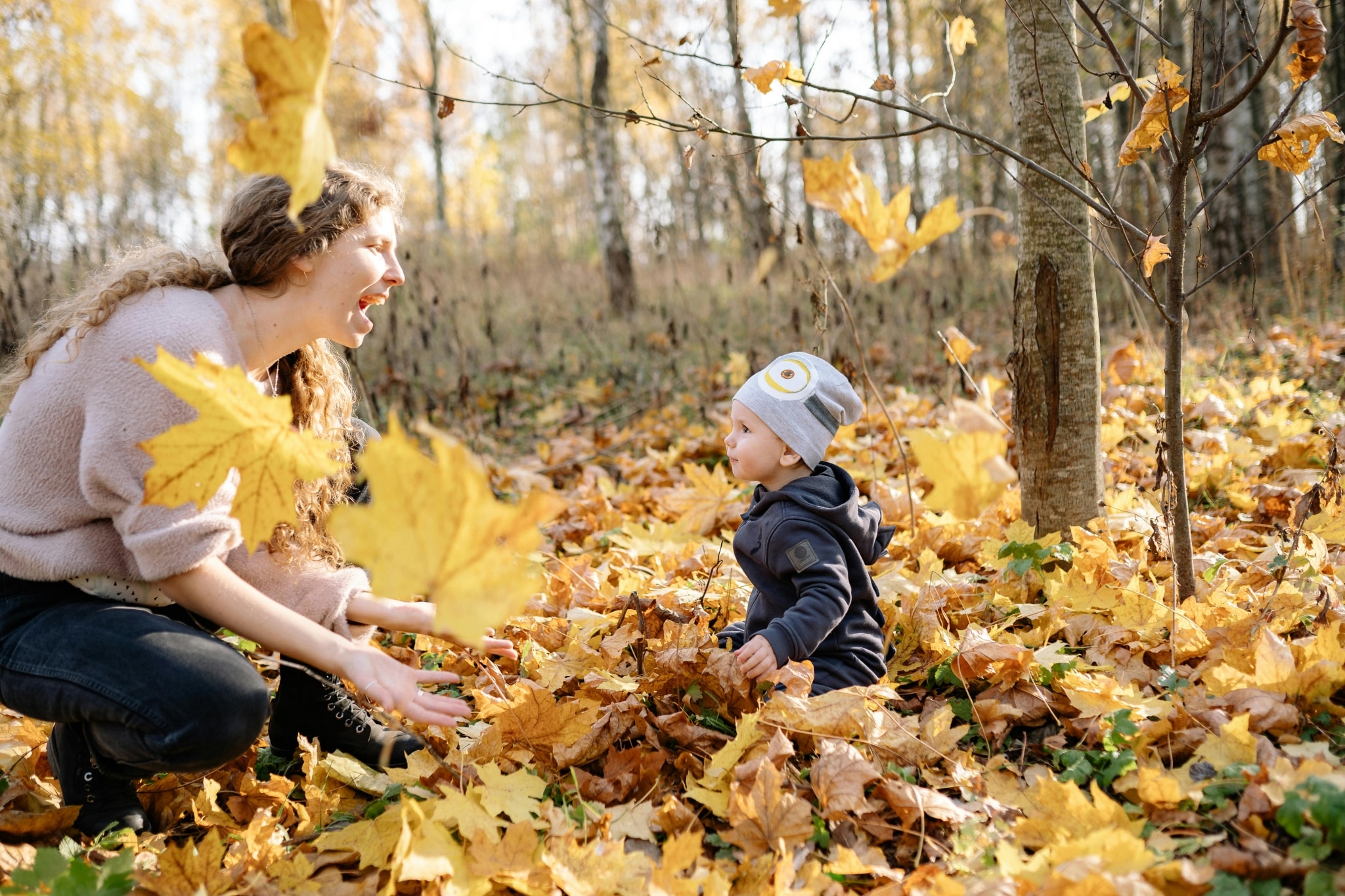 Junge Frau und kleiner Junge spielen im Wald im Herbstlaub.