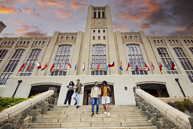 College-Studenten die das Universitätsgebäude verlassen und die Stufen hinuntergehen. Im Hintergrund Gebäude mit Flaggen unterschiedlichster Nationalitäten.
