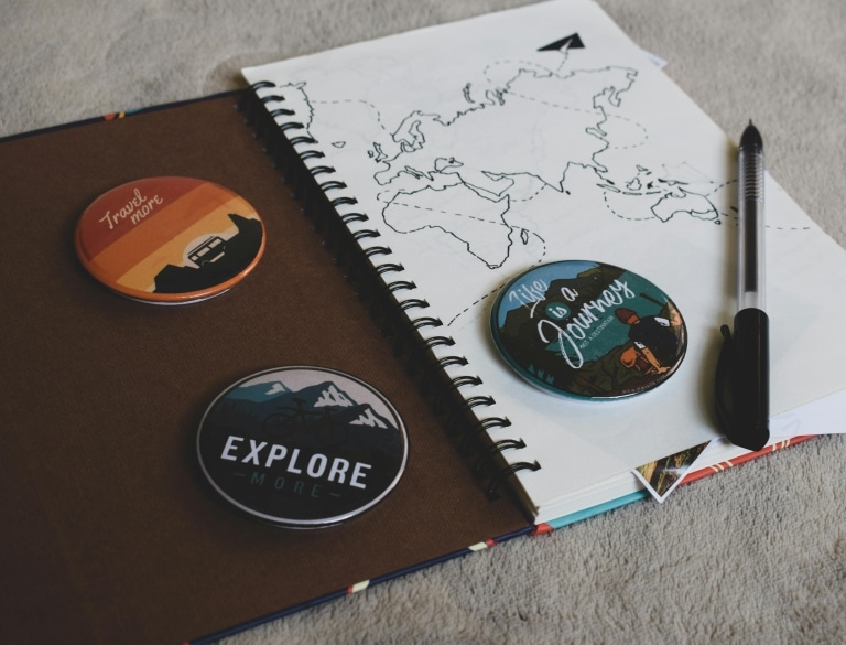 Notizheft mit gezeichneter Weltkarte, schwarzem Kugelschreiber sowie Buttons "Explore", "Life is a Journey! und "Travel more"