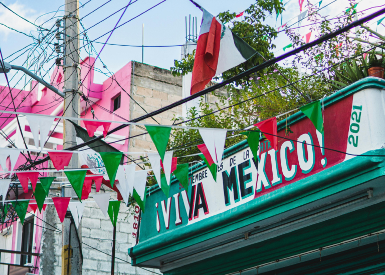 Aufschrift auf einem Lokal "Viva Mexico" sowie kleine Wimpelfahnen in rot, grün und weiß, die über der Straße hängen.